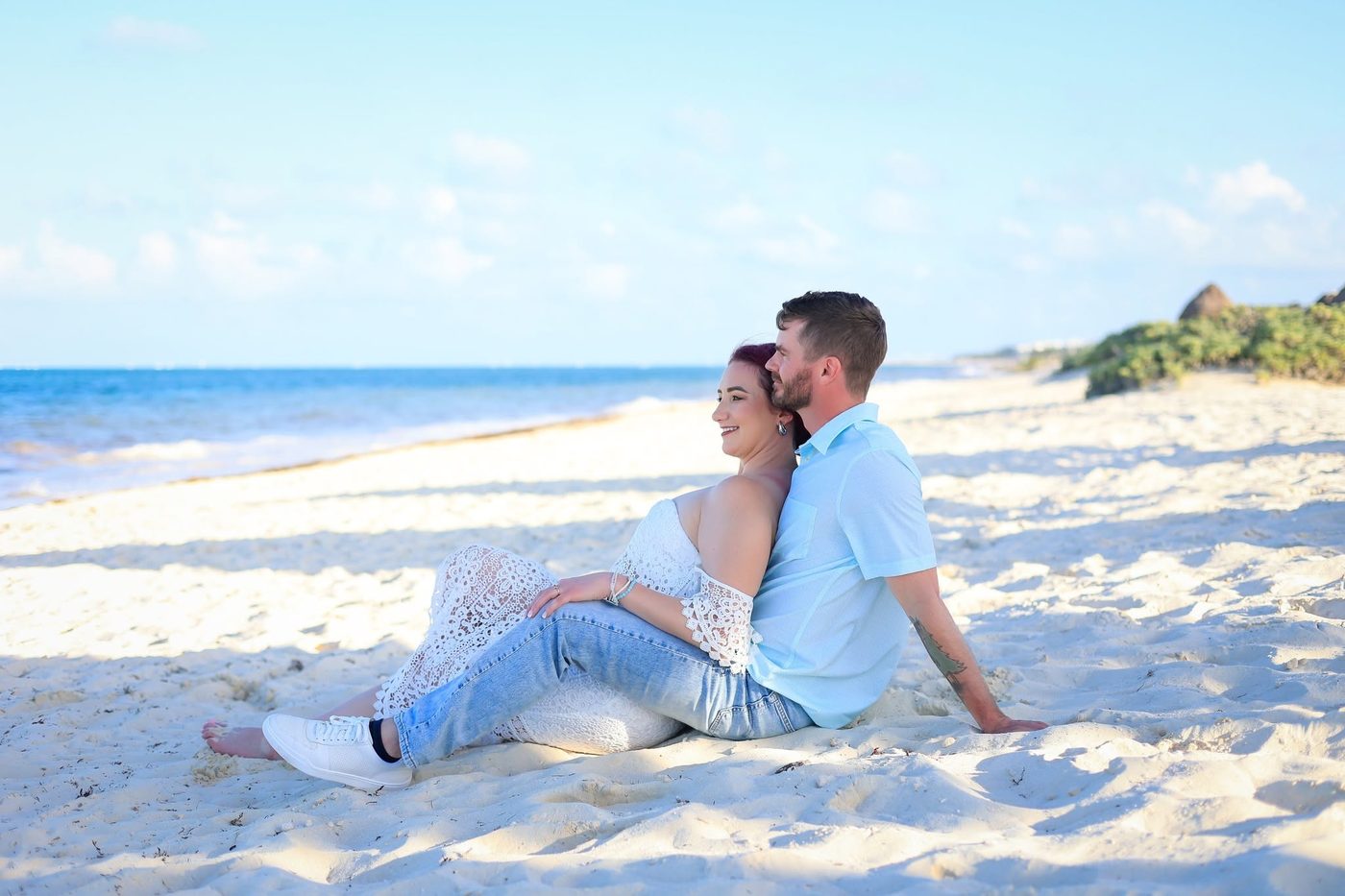 Jackie and Jered sitting together on white sand looking out at the turquoise water